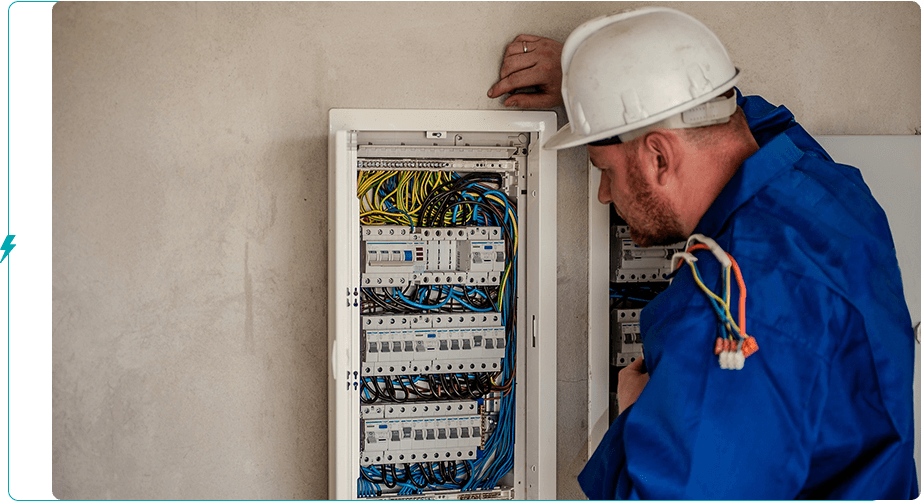 A man in white hard hat looking at an electrical panel.